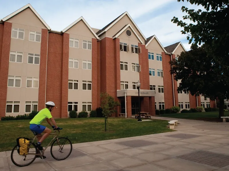 A cyclist riding on a path in front of a dorm.